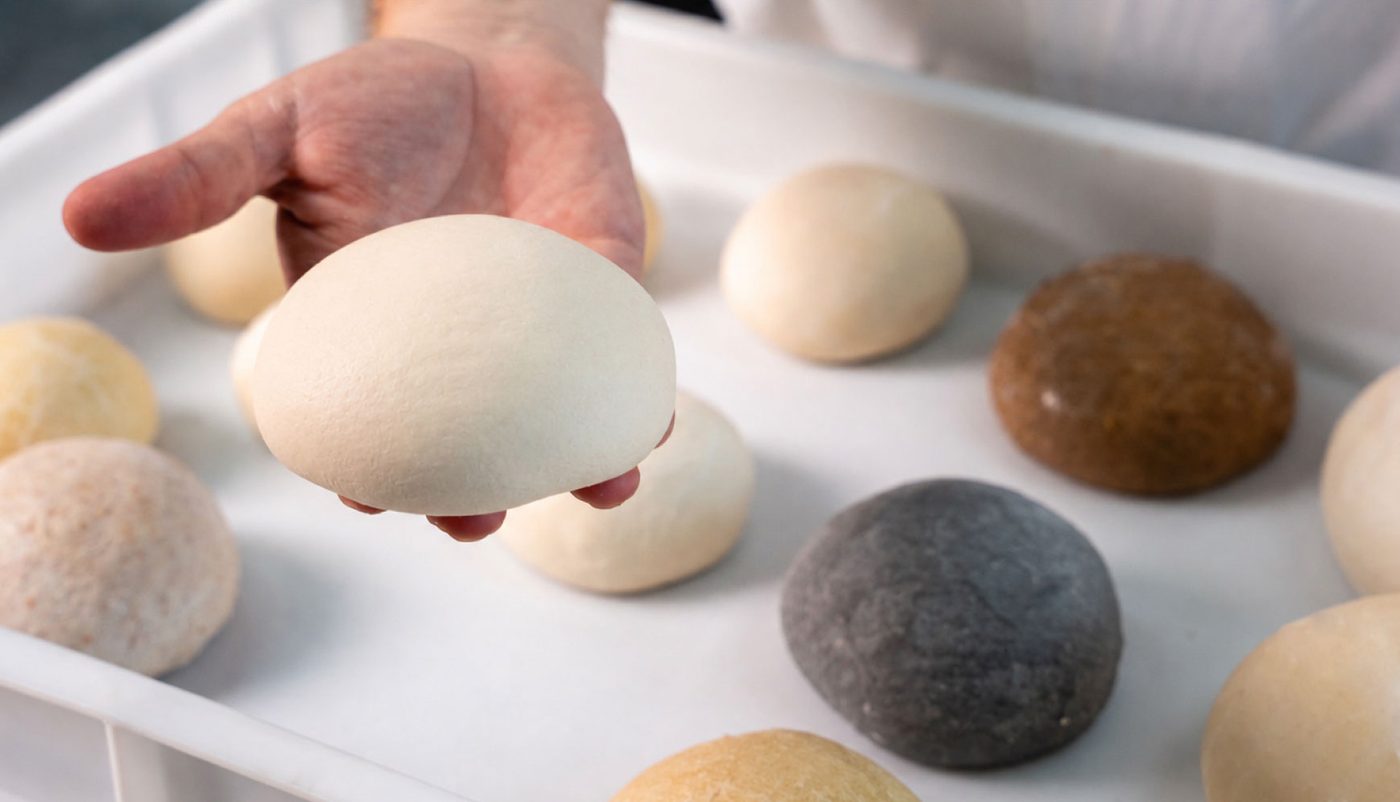 Hand holding a dough ball, with an assortment of different dough types on a tray