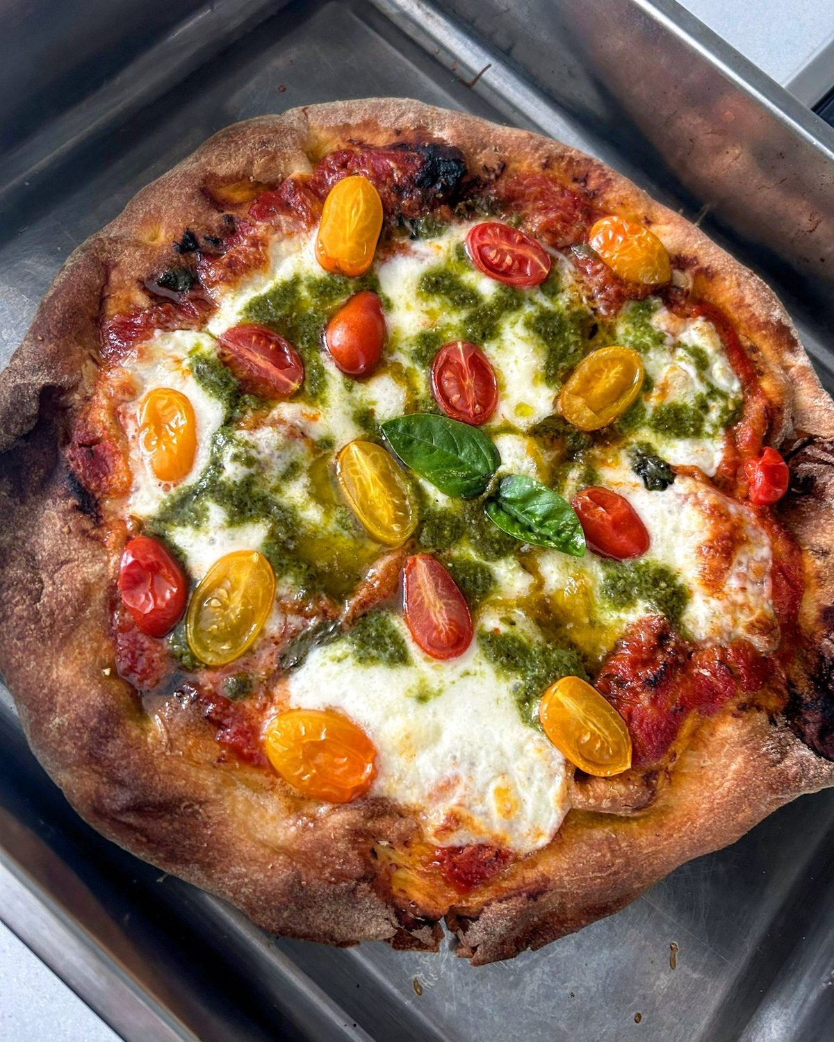 Round pizza base topped with mozzarella, pesto and cherry tomatoes